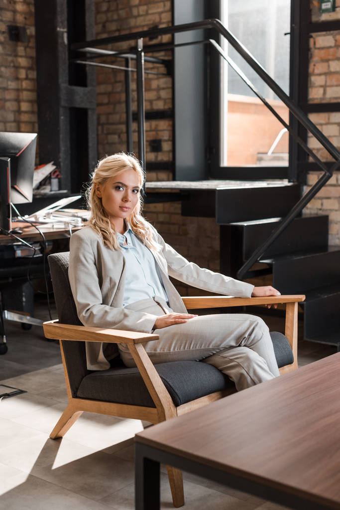 привлекательная задумчивая деловая женщина, сидящая в кресле и смотрящая в камеру
 - Фото, изображение