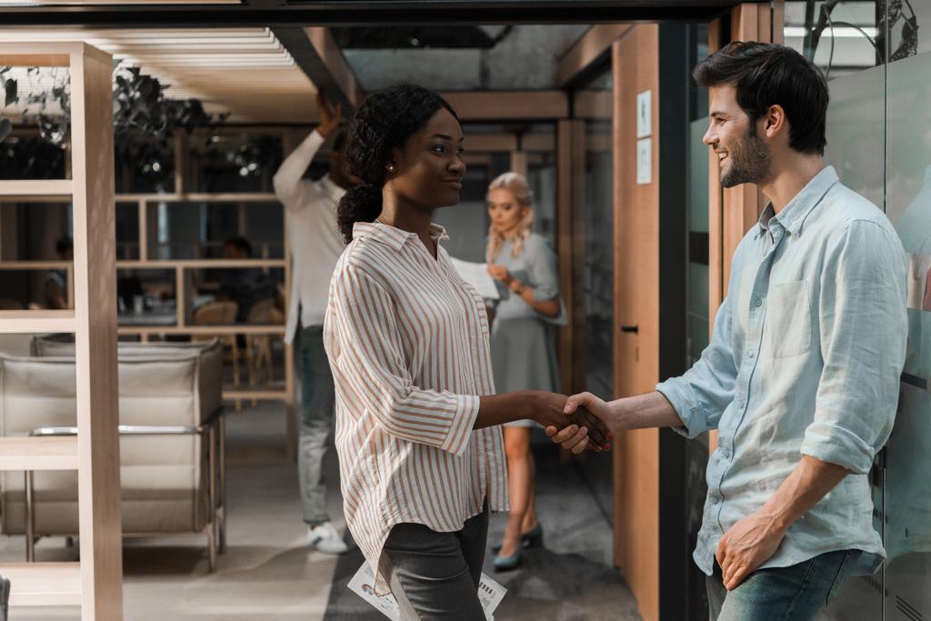 happy african american businesswoman shaking hands with smiling colleague in office - Photo, Image