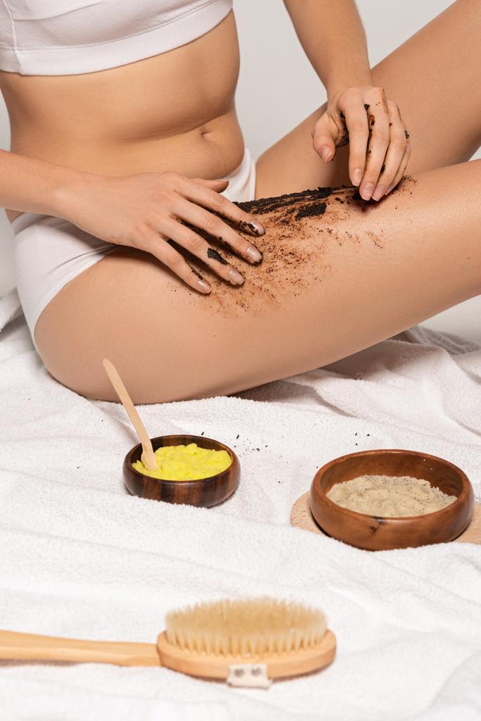 vista cortada da menina com diferentes esfregaços e escova de massagem aplicando esfregaço de café nas pernas
 - Foto, Imagem