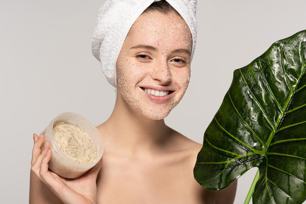 χαμογελαστό κορίτσι με πετσέτα στο κεφάλι κρατώντας πράσινο φύλλο και πλαστικό δοχείο με τρίψιμο καρύδας, απομονώνονται σε γκρι - Φωτογραφία, εικόνα