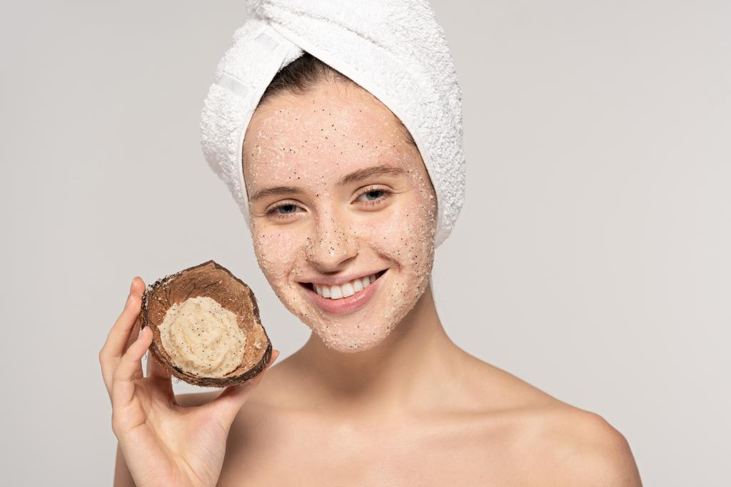 smiling woman with towel on head holding coconut shell with scrub, isolated on grey - Photo, Image