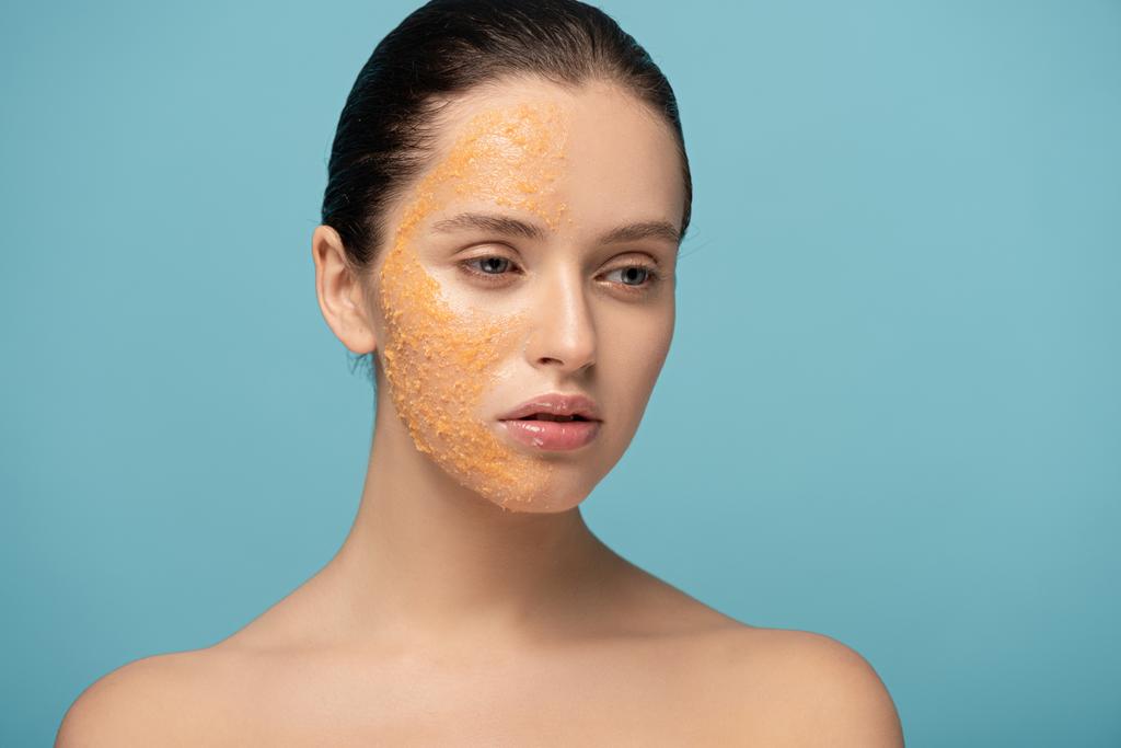 atraktivní dívka nanášení žlutého cukru exfoliant na obličej, izolované na modré - Fotografie, Obrázek