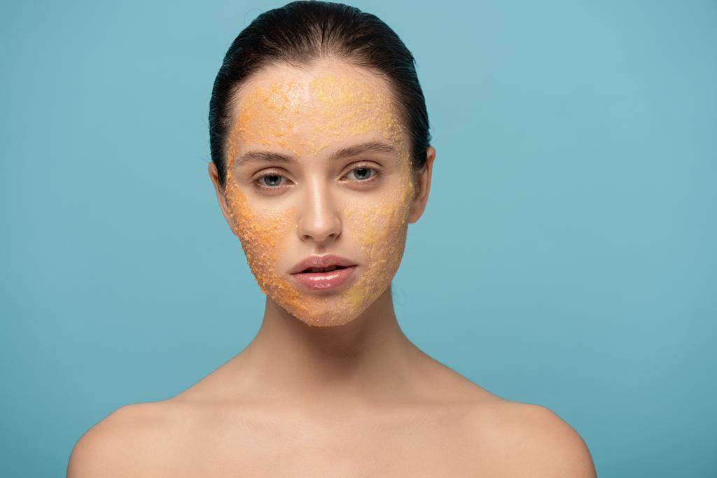 mooi meisje van toepassing gele suiker exfoliant op gezicht, geïsoleerd op blauw - Foto, afbeelding