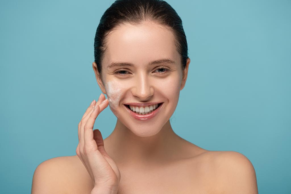 beautiful cheerful woman applying cleansing foam on face, isolated on blue - Photo, Image
