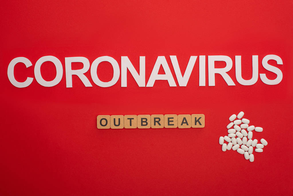 Κάτοψη του επιστολόχαρτου coronavirus και ξέσπασμα σε ξύλινους κύβους κοντά σε χάπια σε κόκκινο φόντο - Φωτογραφία, εικόνα