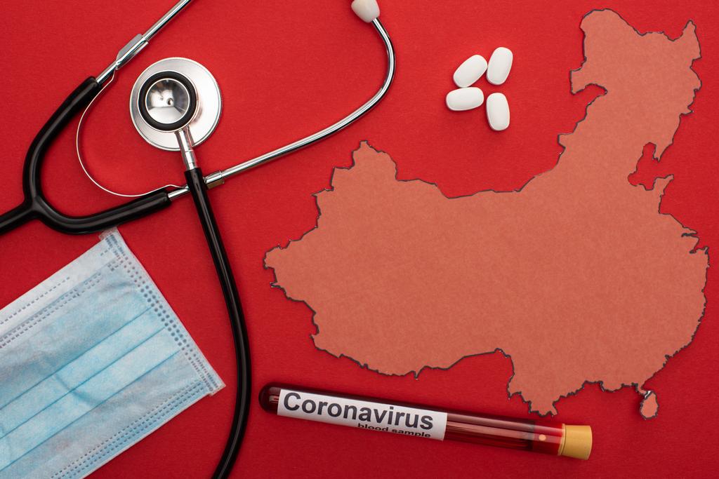 Top view of stethoscope, medical mask and test tube with coronavirus lettering near map of china on red background - Photo, Image