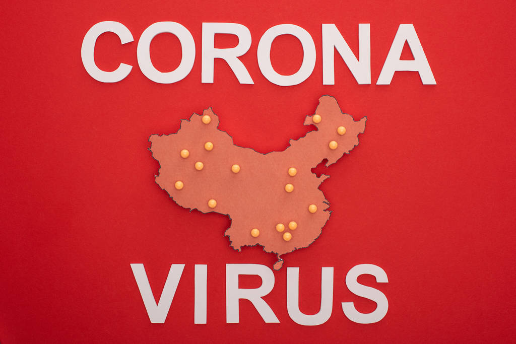 Horní pohled na porcelánovou mapu se žlutými tlačnými špendlíky a koronavirovými písmeny na červeném pozadí - Fotografie, Obrázek