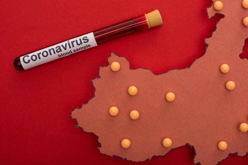 Top view of map of china with push pins and test tube with blood sample and coronavirus lettering on red background - Photo, Image