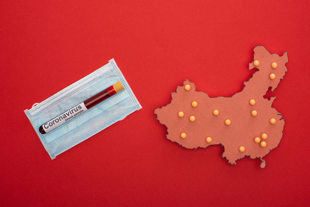 Κάτοψη της διάταξης του χάρτη της Κίνας με γράμματα coronavirus στο δοκιμαστικό σωλήνα και ιατρική μάσκα σε κόκκινο φόντο - Φωτογραφία, εικόνα