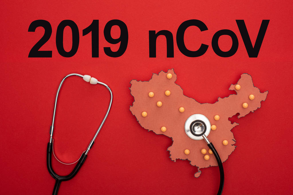 Bovenaanzicht van stethoscoop op lay-out van porseleinkaart met 2019 ncov belettering op rode achtergrond - Foto, afbeelding