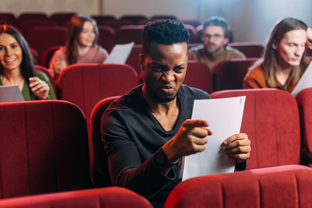 Kızgın Afrikalı Amerikalı aktör oyuncularla kırmızı sandalyelerde prova yapıyor. - Fotoğraf, Görsel