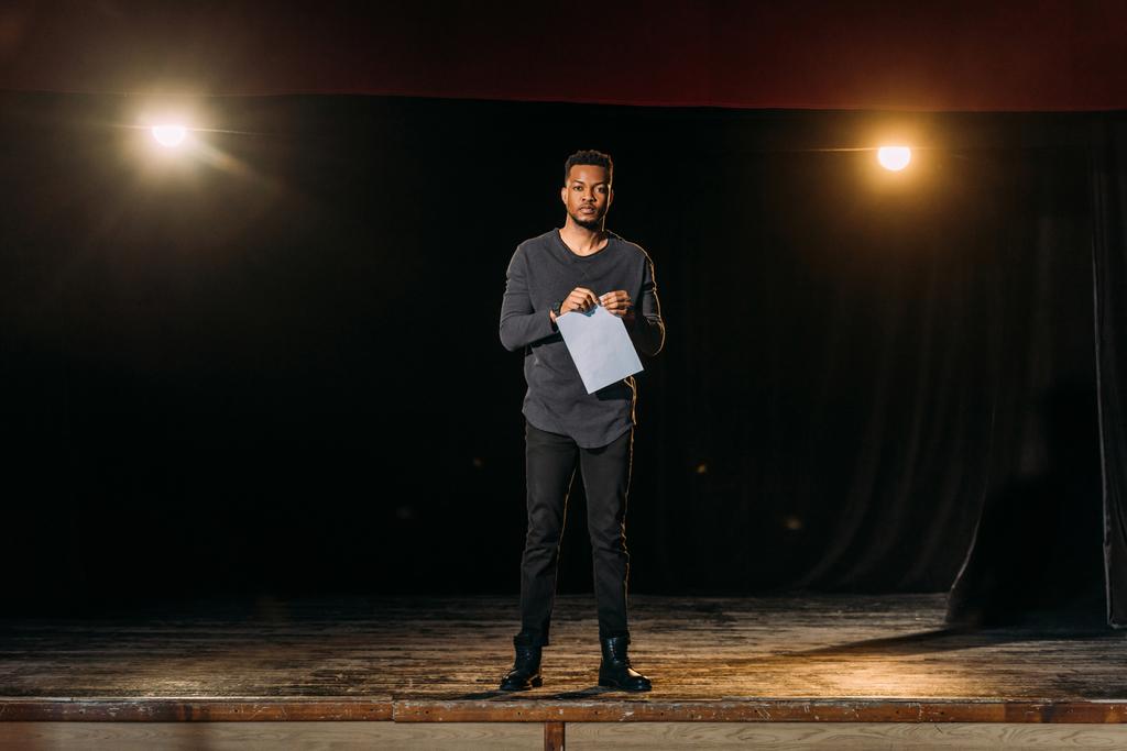 ator afro-americano segurando cenário e de pé no palco durante o ensaio
  - Foto, Imagem