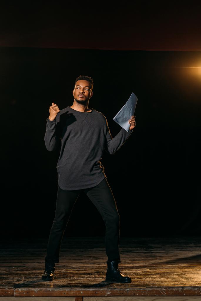 Afrykański amerykański aktor trzymający scenariusz i stojący na scenie podczas próby w teatrze - Zdjęcie, obraz