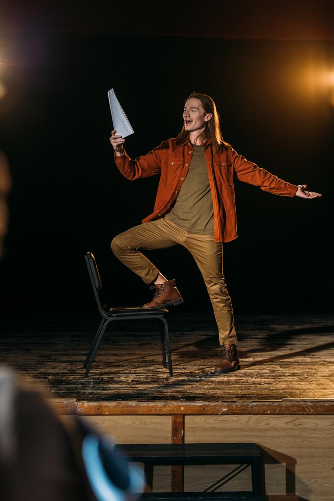 apuesto actor con guion jugando en el escenario durante el ensayo en el teatro
 - Foto, Imagen