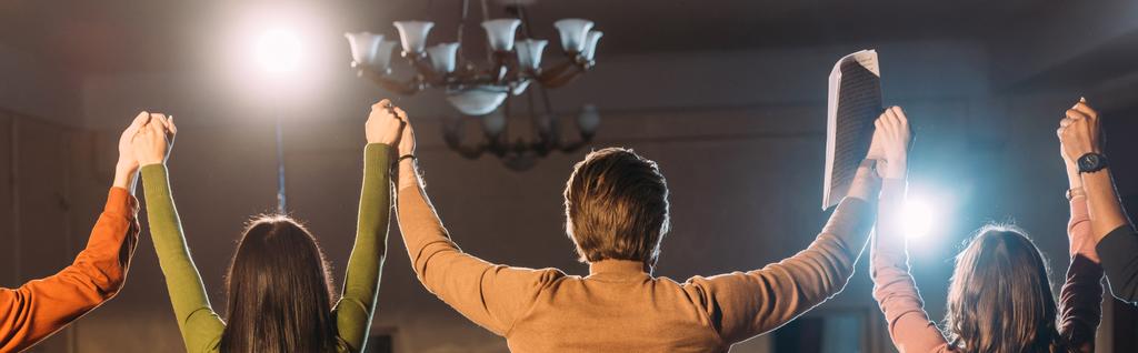 panoramatický záběr herců a hereček s rukama nad hlavou a dramatickým osvětlením - Fotografie, Obrázek