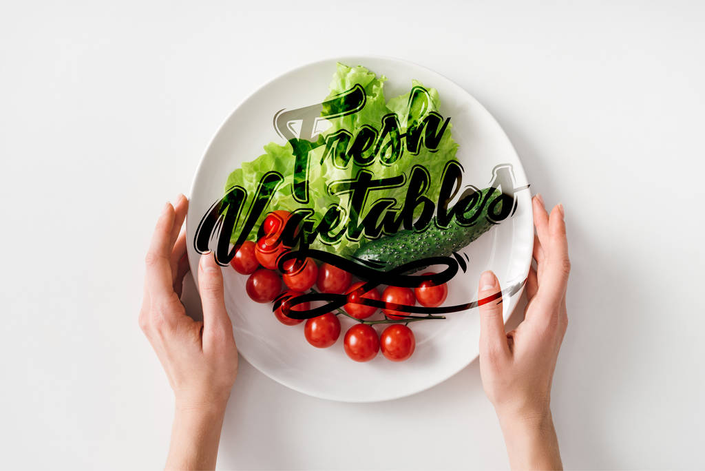 Bovenaanzicht van vrouw met bord met rauwe groenten op witte achtergrond - Foto, afbeelding