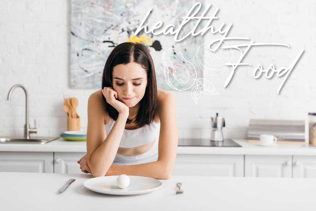 Pensive sportovkyně při pohledu na vejce na kuchyňském stole v blízkosti zdravé jídlo ilustrace - Fotografie, Obrázek