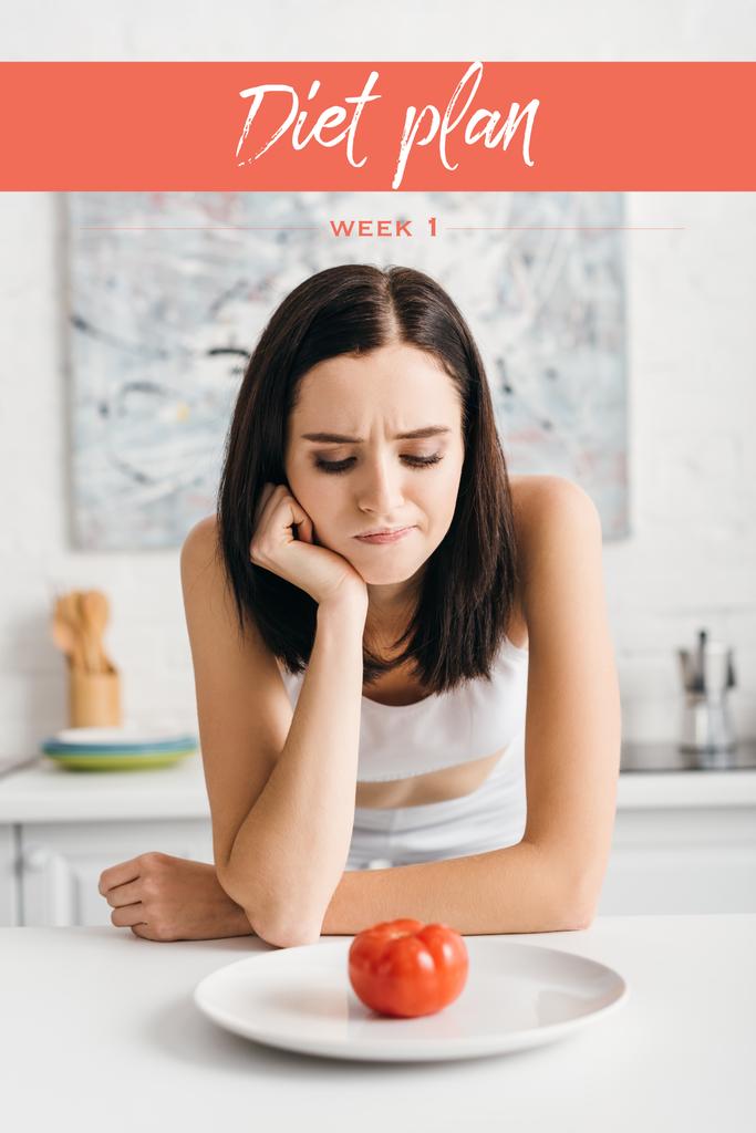Pensive sportswoman looking at ripe tomato on plate on table near diet plan lettering - Photo, Image