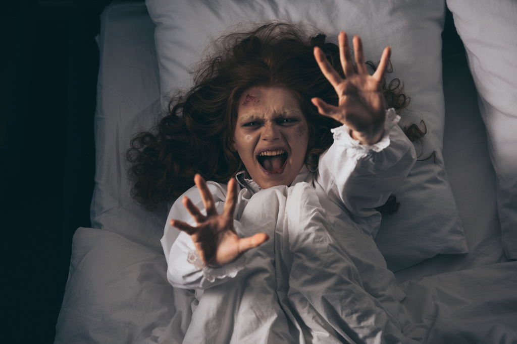 Gecelik giymiş, yatakta bağıran ve el kol hareketi yapan takıntılı bir kız. - Fotoğraf, Görsel