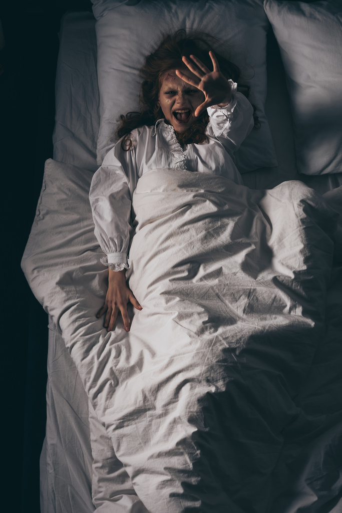 Вид сверху одержимой девушки в ночном халате, кричащей и жестикулирующей в постели
 - Фото, изображение