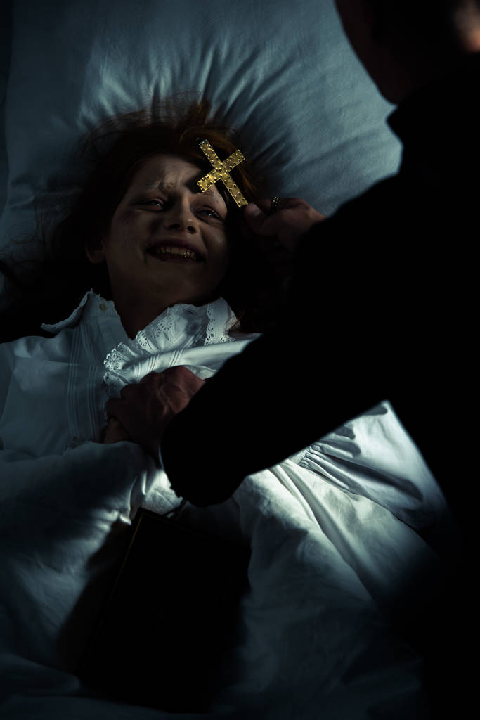 exorcista segurando cruz sobre demônio feminino na cama
 - Foto, Imagem
