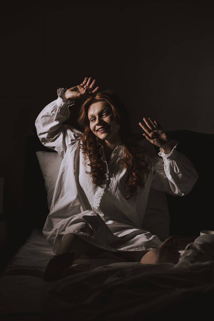 schrecklich besessen lächelndes Mädchen im Nachthemd im Bett sitzend - Foto, Bild