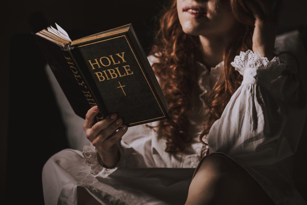 vista recortada de demonio femenino en camisón leyendo la sagrada biblia en la cama
 - Foto, imagen