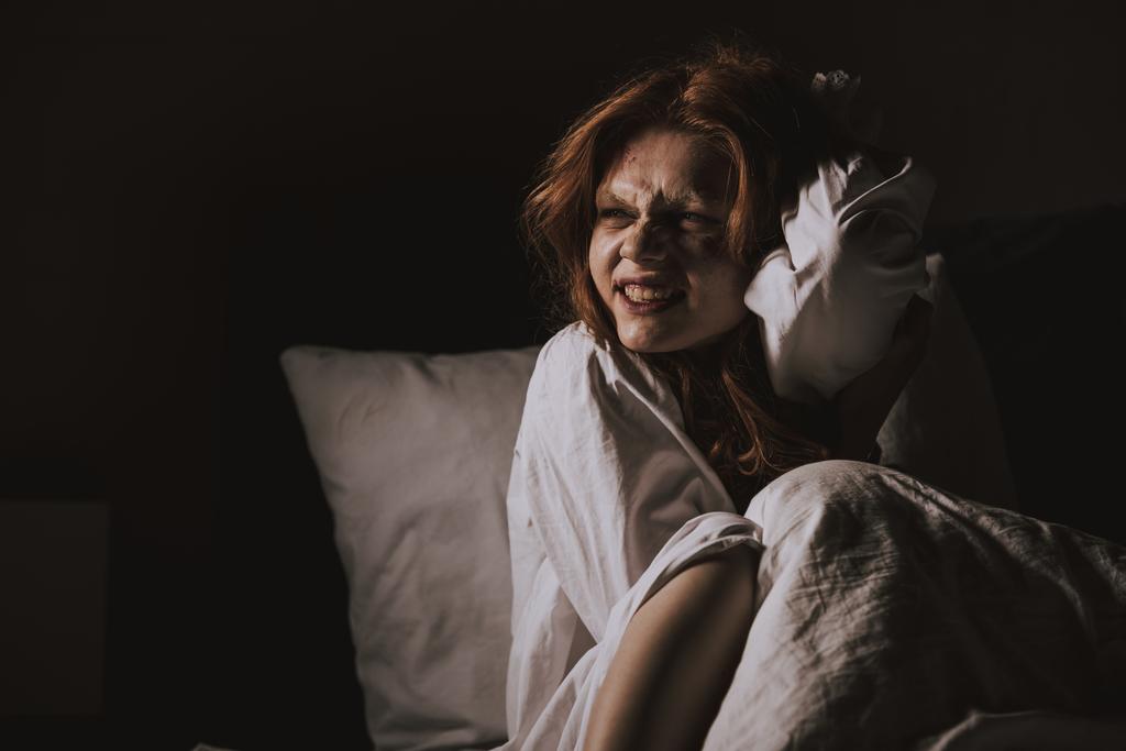 vrouw lachende duivel in nachtjapon zitten in bed - Foto, afbeelding