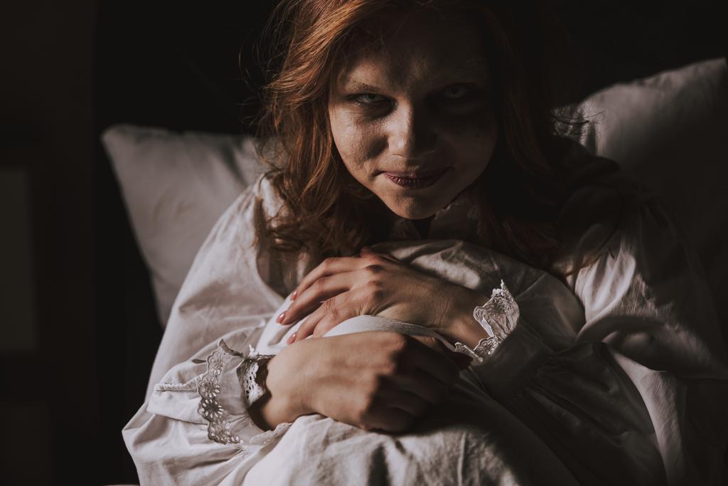 demoniczne uśmiechnięta kobieta w koszuli nocnej siedzi w łóżku - Zdjęcie, obraz