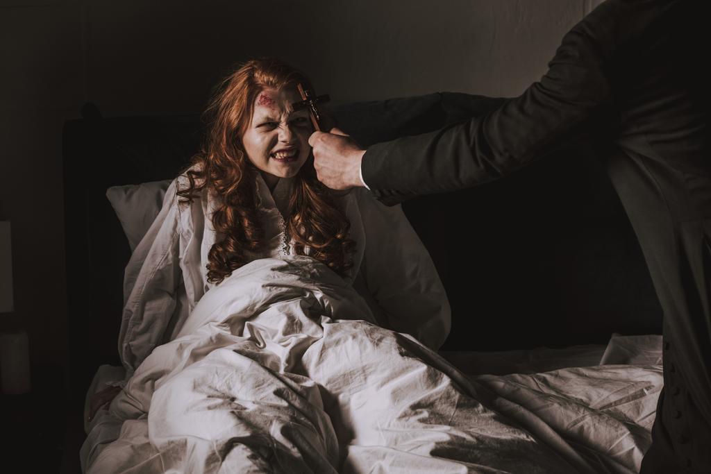 ördögűző tartja kereszt előtt megszállott lány az ágyban - Fotó, kép