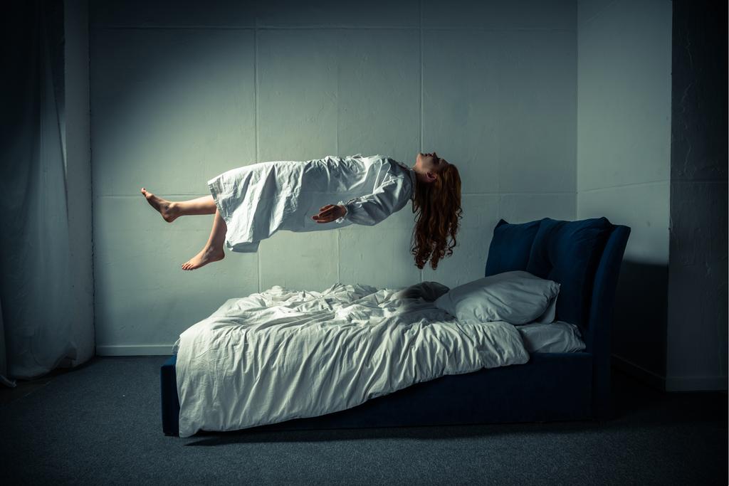 δαιμονικό κορίτσι με νυχτικό αιωρείται πάνω από το κρεβάτι - Φωτογραφία, εικόνα