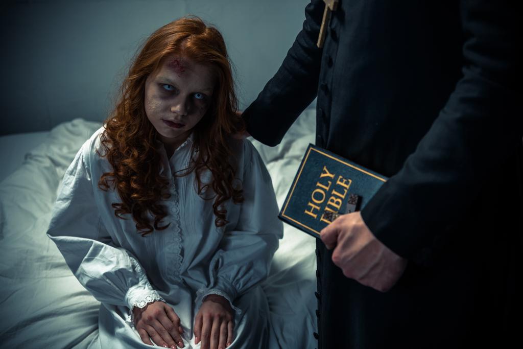 Exorzist hält Bibel und umarmt dämonisches Mädchen im Schlafzimmer  - Foto, Bild