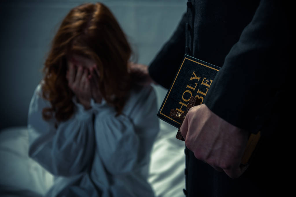 exorcist houden bijbel en knuffelen huilen meisje in slaapkamer  - Foto, afbeelding