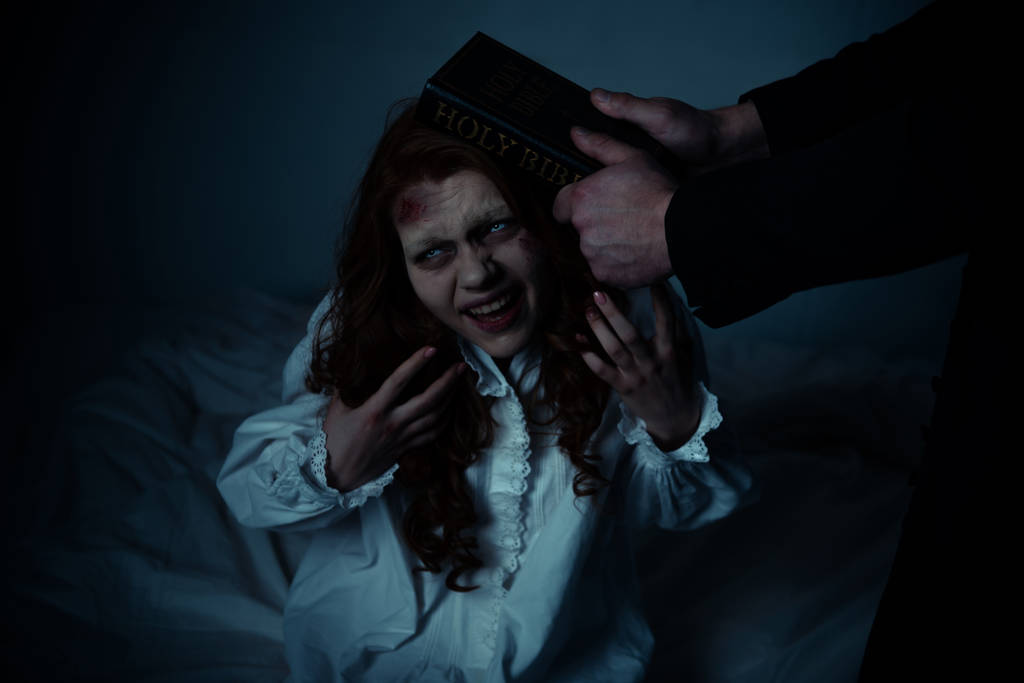 exorcist houden bijbel in de buurt hoofd van geobsedeerd meisje in slaapkamer  - Foto, afbeelding