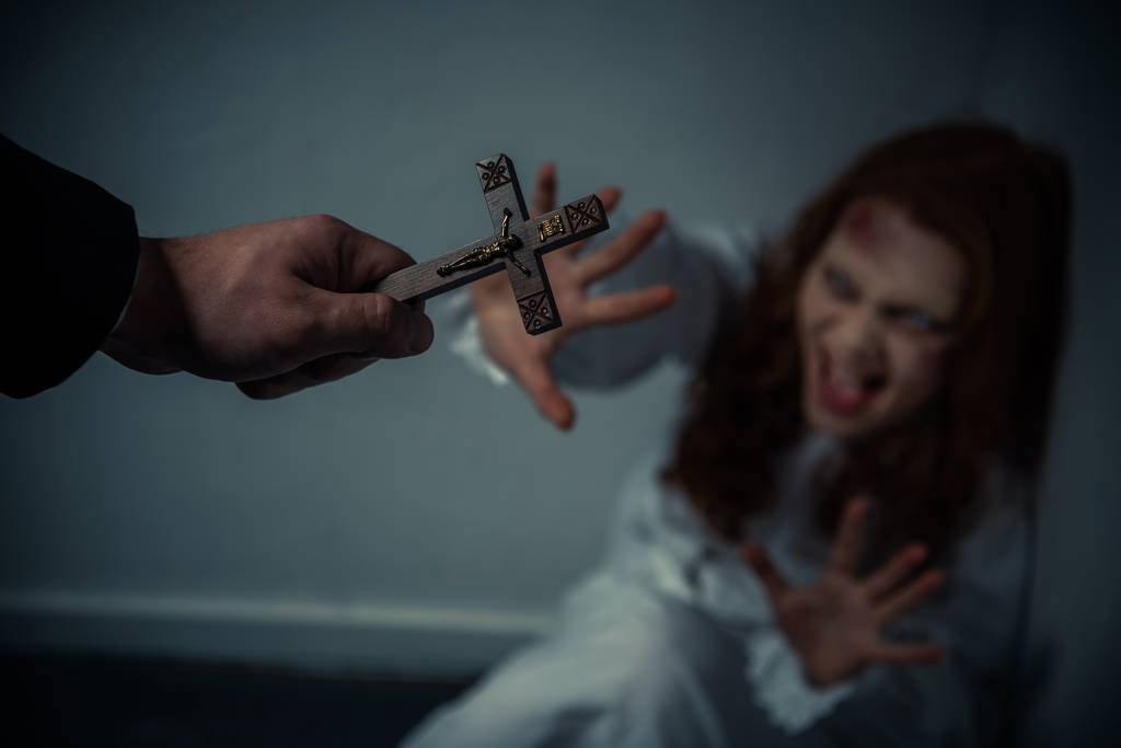 selektivní zaměření vymítače ďábla držícího kříž před křičící posedlou dívkou - Fotografie, Obrázek