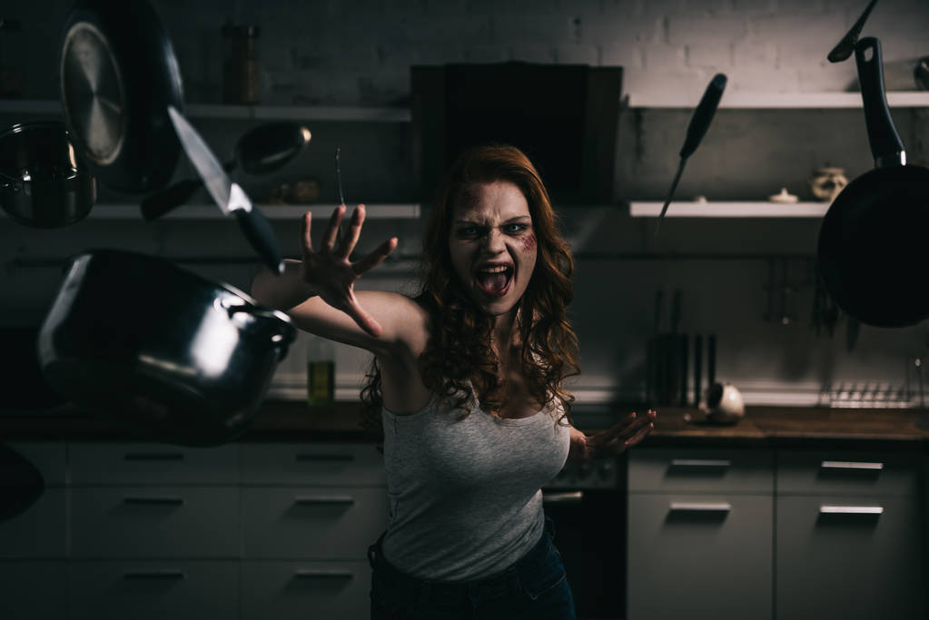 悪魔的な叫びの女の子ジェスチャーで台所で台所用品を持ち上げ - 写真・画像