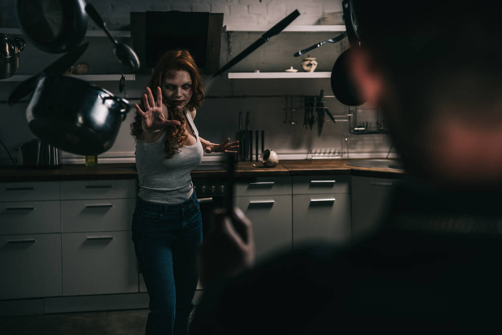 selective focus of female demon with levitating cookware and exorcist with cross in kitchen - Photo, Image