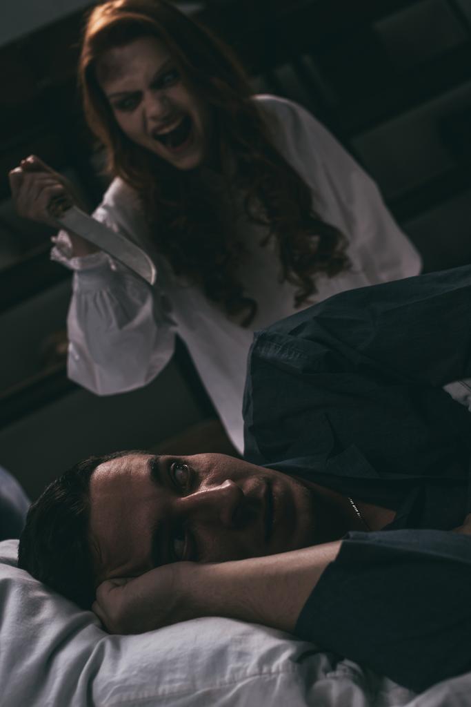 posedlá křičící dívka s nožem stojící nad vystrašeným mužem v posteli - Fotografie, Obrázek