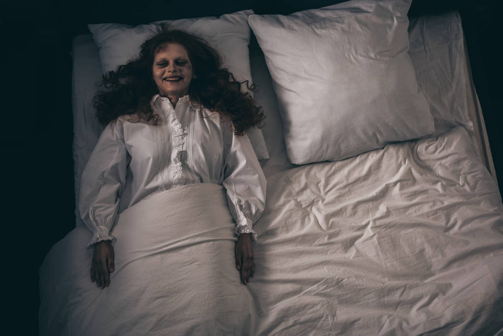 ベッドの上に寝そべっている夜のガウンに身を包んだ不気味な笑顔の鬼 - 写真・画像
