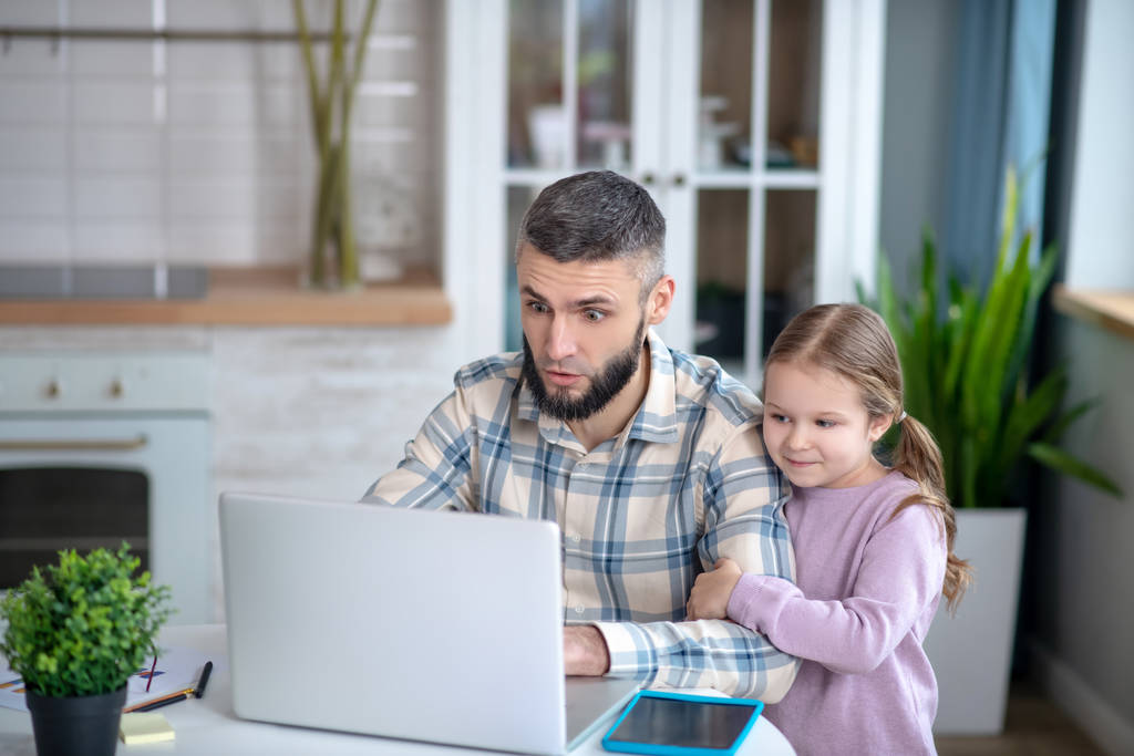 Jovem pai de cabelos escuros e menina criança olhando para um laptop
. - Foto, Imagem