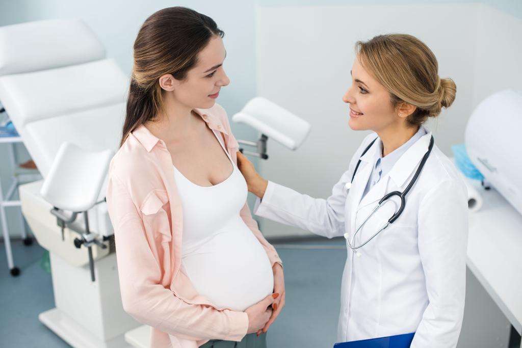 młoda uśmiechnięta kobieta w ciąży po konsultacji z ginekologiem w klinice - Zdjęcie, obraz