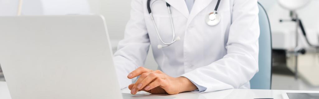 πανοραμικό πλάνο επαγγελματία γιατρού που εργάζεται σε φορητό υπολογιστή στην κλινική   - Φωτογραφία, εικόνα