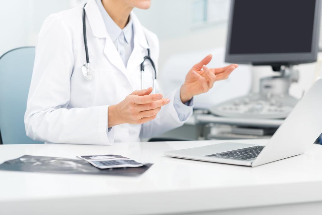 professionele vrouwelijke arts werken op laptop in kliniek met echografie scanner - Foto, afbeelding