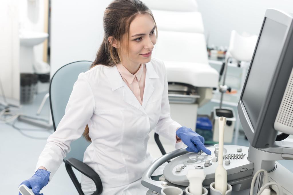 молодой улыбающийся врач работает с ультразвуковым сканером в клинике
 - Фото, изображение