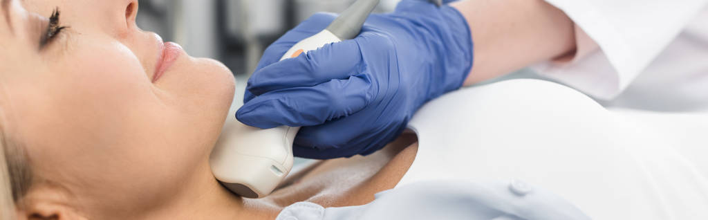 обрезанный вид врача, осматривающего щитовидную железу пациентки с помощью ультразвукового сканирования в клинике, панорамный снимок
  - Фото, изображение
