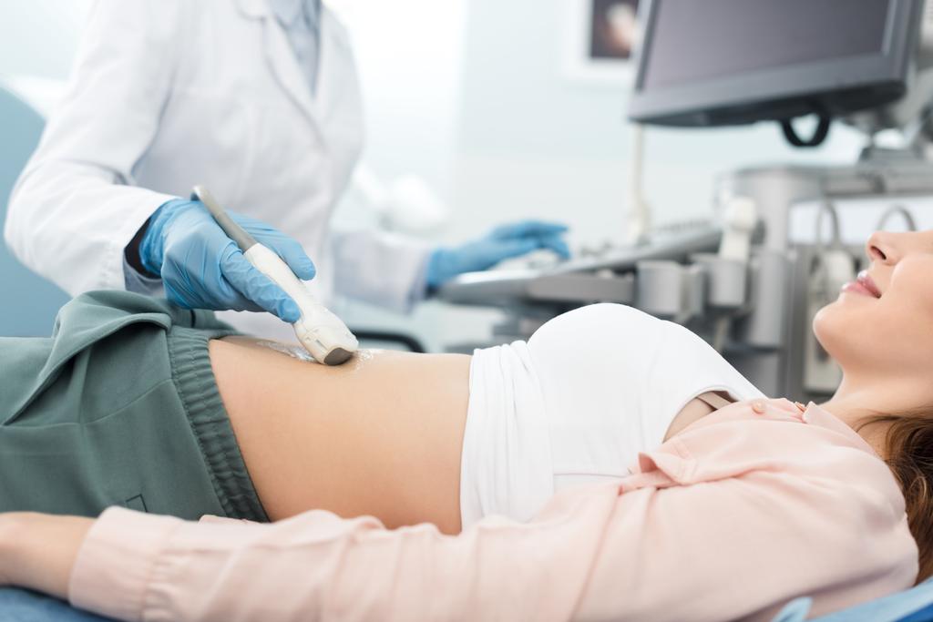 vista recortada del médico examinando el estómago de la paciente femenina con ecografía en la clínica
  - Foto, Imagen