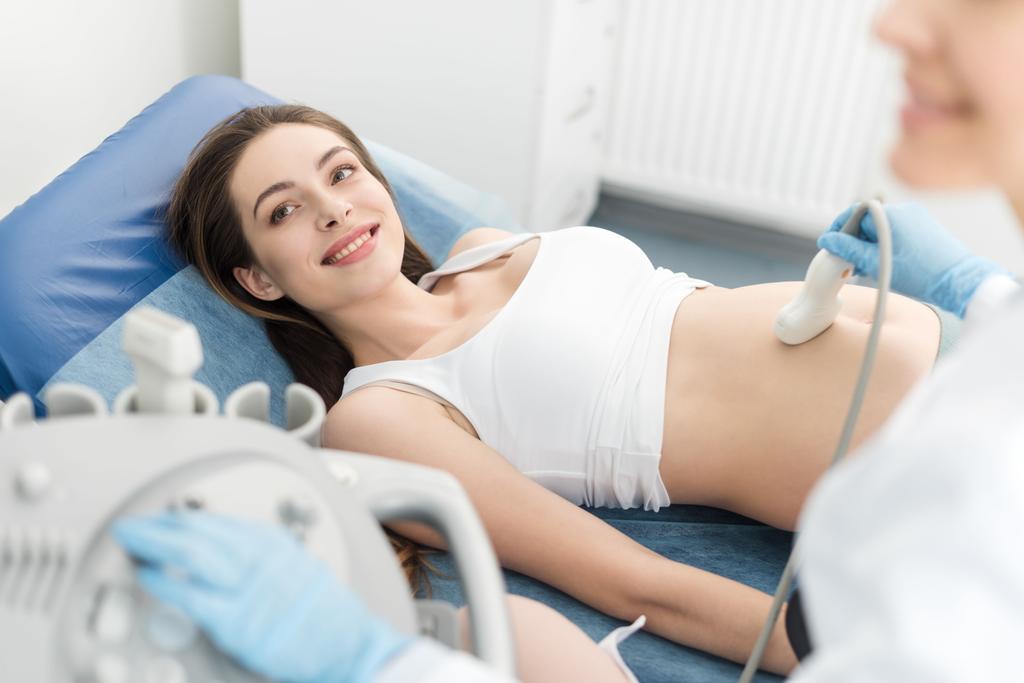 Arzt untersucht Bauch lächelnder Schwangerer mit Ultraschall in Klinik - Foto, Bild