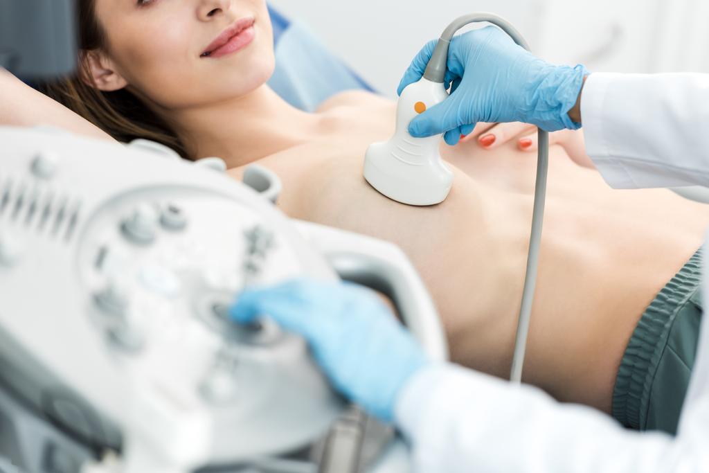 超音波スキャナーを使用して患者の乳房検査を行う医師のクロップドビュー - 写真・画像