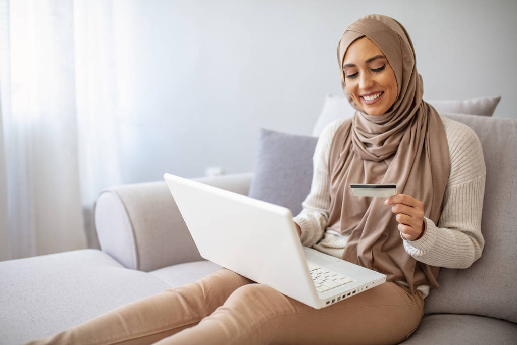 Content Arab Woman Shopping Online Being At Home. Online shopping. Beautiful young muslim woman showing a credit card with laptop. Smiling young muslim girl online shopping at home - Photo, Image