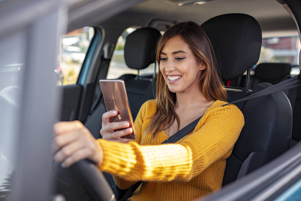 車内の女性携帯電話を保持.少女は交通渋滞の中でテキストメッセージを送っている。若い女性ドライバーが車輪のスマートフォンを使っている。若い女性は、携帯電話で車の中で、彼女のテキストメッセージや彼女のナビゲーションをチェックします - 写真・画像